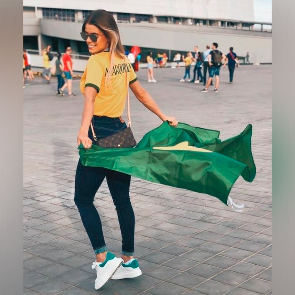 Mulher segurando bandeira do Brasil e usando camiseta amarela da seleção brasileira